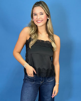 A woman modeling a black satin strapless top with lace trim and dark blue wide-leg jeans