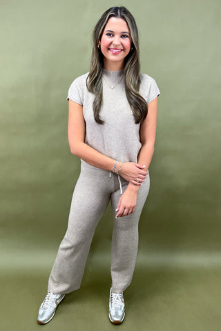 Woman wearing a gray outfit with white sneakers on a green background
