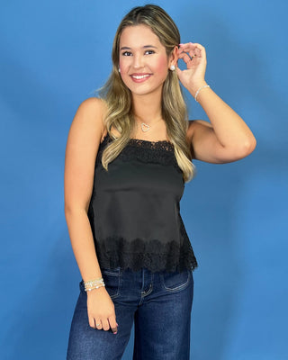 A woman modeling a black satin strapless top with lace trim and dark blue wide-leg jeans