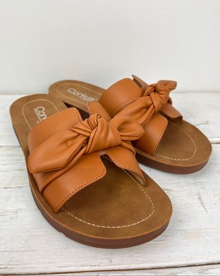 Pair of brown sandals with bow details on a white wooden surface
