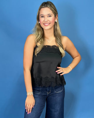 A woman modeling a black satin strapless top with lace trim and dark blue wide-leg jeans