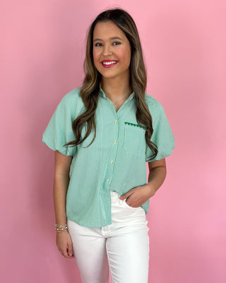 Woman wearing a green checkered shirt with a logo on a pink background
