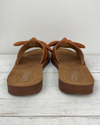 Pair of brown sandals on a light wooden floor with a white background