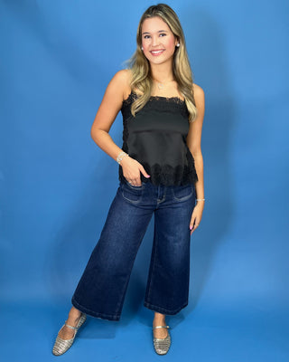 A woman modeling a black satin strapless top with lace trim and dark blue wide-leg jeans