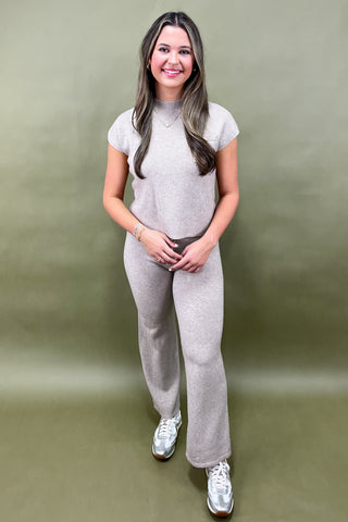 Woman wearing a gray outfit with white sneakers against a green background