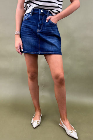 Person wearing a blue denim skirt with a plain background