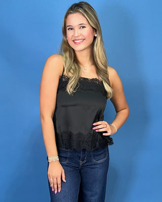 A woman modeling a black satin strapless top with lace trim and dark blue wide-leg jeans
