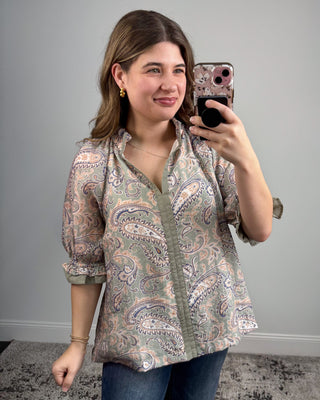 Woman taking a mirror selfie wearing a patterned blouse against a plain background