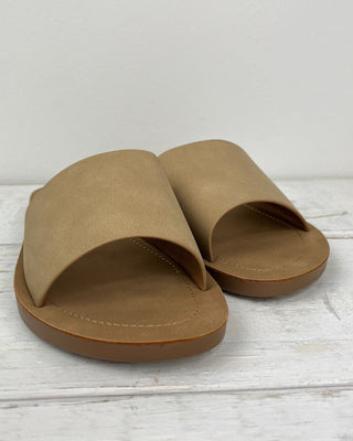 Tan sandal on a light wooden surface with a white background
