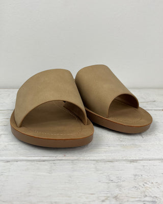 Pair of tan sandals on a light wooden surface with a white background