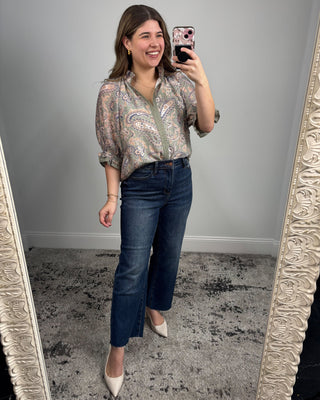 Woman taking a mirror selfie wearing a patterned blouse and blue jeans.