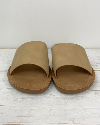Pair of tan slides on a light wooden surface with a white background
