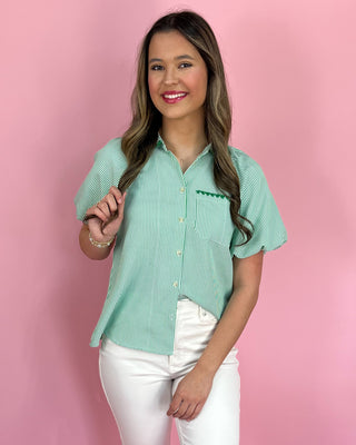 Woman wearing a green and white striped shirt with a logo on a pink background