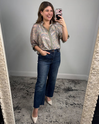 Woman taking a mirror selfie wearing a patterned blouse and jeans.
