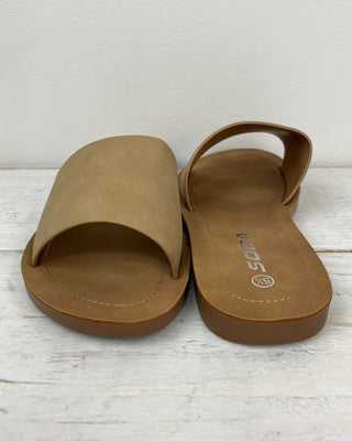 Pair of tan sandals on a white wooden surface with a light gray background