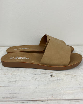 Pair of brown sandals with 'Soda' branding on a light wooden surface.