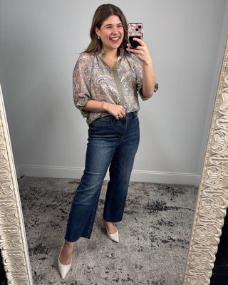 Woman taking a mirror selfie wearing a patterned blouse and jeans.