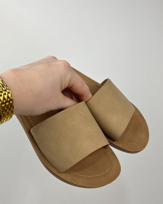 Beige sandal held by a hand on a light gray background