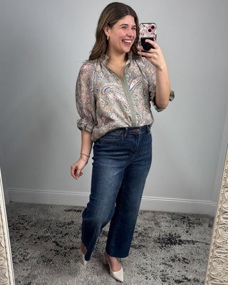Woman taking a mirror selfie wearing a patterned blouse and blue jeans.