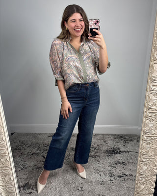 Woman taking a mirror selfie wearing a patterned blouse and blue jeans.