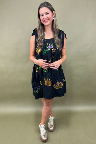 Woman wearing a black dress with colorful embroidery against a plain background