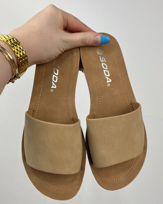 Tan sandals held by a hand with gold bracelet on a white background