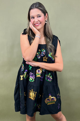 Woman wearing a black dress with colorful embellishments against a green background