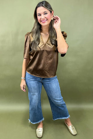 Woman wearing a brown top and blue jeans against a green background
