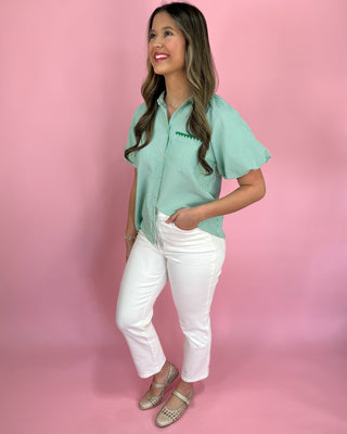 Woman wearing a green patterned shirt and white pants on a pink background