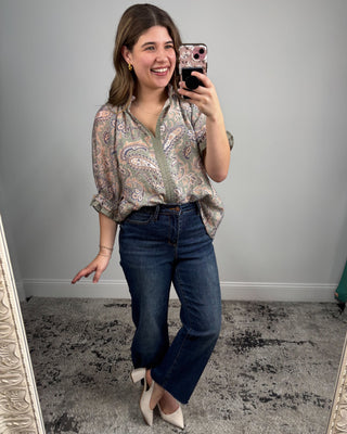 Woman taking a mirror selfie wearing a patterned blouse and jeans.