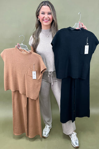 Woman holding two clothing items on hangers against a plain background