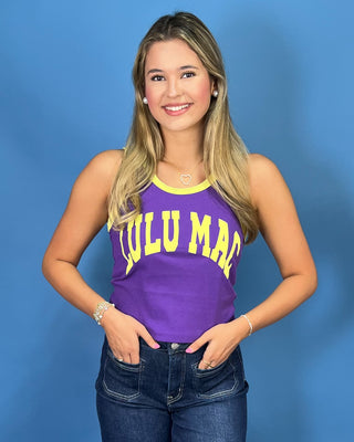 A woman modeling a purple sleeveless tank top with yellow trim and 'LULU MAC' printed in yellow across the front, paired with dark blue jeans