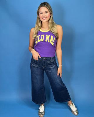 A woman modeling a purple sleeveless tank top with yellow trim and 'LULU MAC' printed in yellow across the front, paired with dark blue jeans