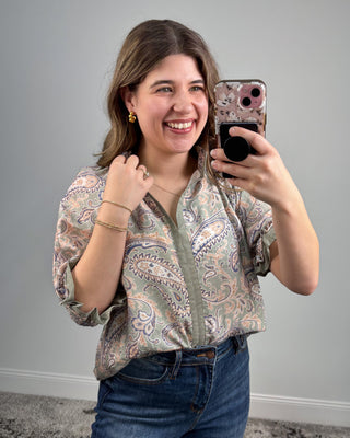 Woman taking a mirror selfie wearing a patterned blouse and jeans against a plain background