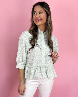 Woman wearing a light green patterned blouse with ruffled details against a pink background