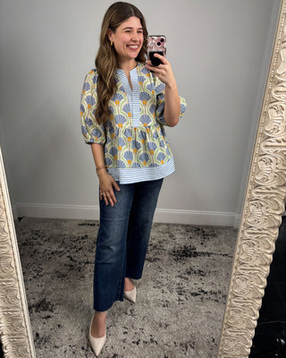 Woman taking a mirror selfie wearing a patterned top and blue jeans.