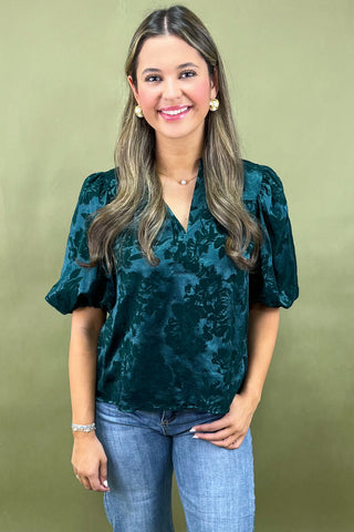 Woman wearing a green velvet top and blue jeans against a green background