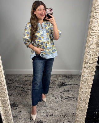 Woman taking a mirror selfie wearing a patterned blouse and jeans.