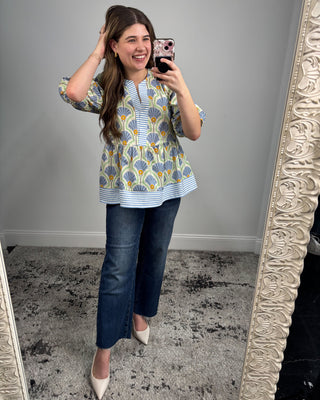 Woman taking a mirror selfie wearing a patterned blouse and jeans.