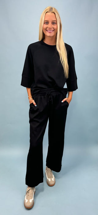 Woman wearing a black outfit with wide-leg pants on a light blue background