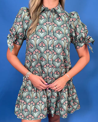 A woman wearing a short puff-sleeve shirt dress with a green, pink, and beige floral Art Deco pattern