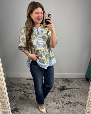 Woman taking a mirror selfie wearing a patterned top and jeans indoors.