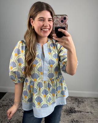 Woman taking a mirror selfie wearing a patterned blouse with a plain background