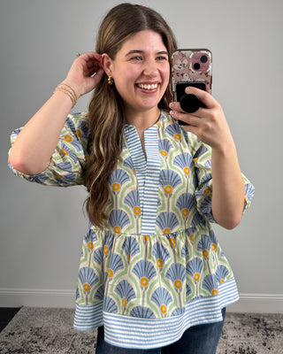 Woman taking a mirror selfie wearing a patterned blouse with a gray background
