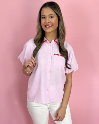 Woman wearing a pink and white striped shirt with red accents against a pink background