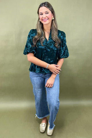 Woman wearing a dark green blouse and blue jeans against a gold background