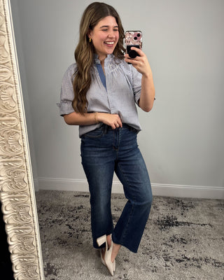 Woman taking a mirror selfie wearing a checkered shirt and blue jeans.