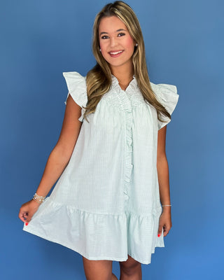 Woman wearing a light blue and white striped dress with ruffled sleeves against a blue background