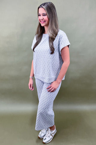 Woman wearing a white patterned outfit against a plain background