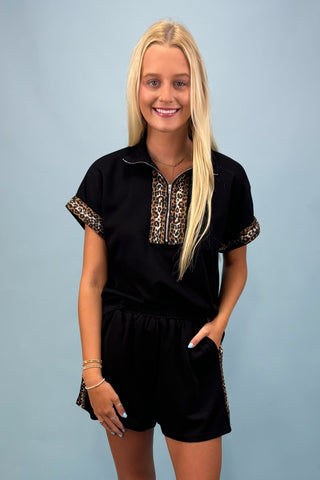 Woman wearing a black outfit with leopard print accents on a light blue background